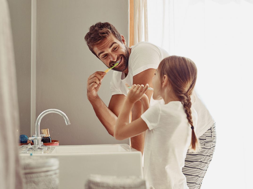 Dad and young daughter brushing their teeth together in the bathroom